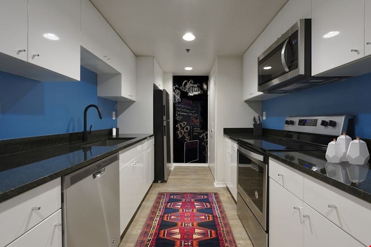 Renovated Package I kitchen with black granite countertops, stainless steel appliances, white cabinetry, blue painted backsplash, and hard surface flooring