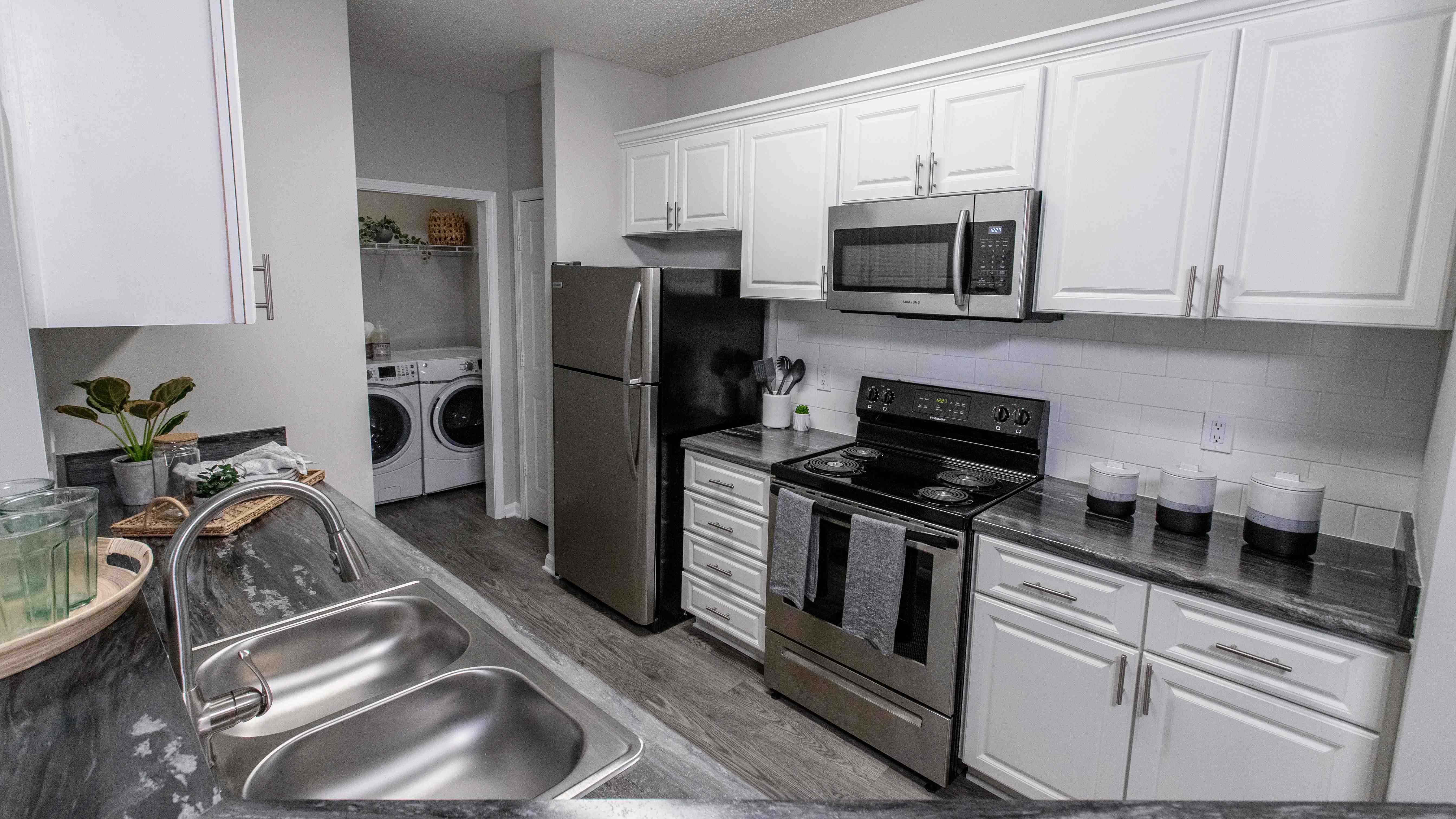 Experience timeless elegance in our updated kitchens, featuring white cabinetry, a modern subway tile backsplash, and wood-style flooring with stainless-steel appliances. 