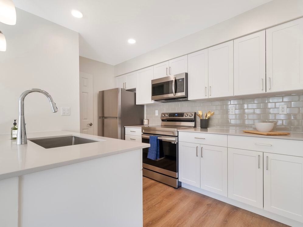 Renovated Package II kitchen with stainless steel appliances, beige quartz countertops, white cabinetry, light grey tile backsplash, and hard surface flooring