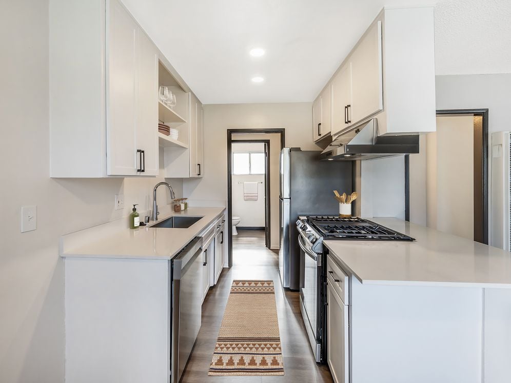 Renovated Package I kitchen with stainless steel appliances, white quartz countertops, white cabinetry, and hard surface flooring (select homes)