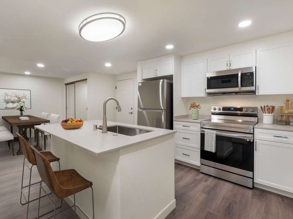 Kitchen with beige quartz countertops, white cabinetry, stainless steel appliances, and hard surface flooring (Select Home)