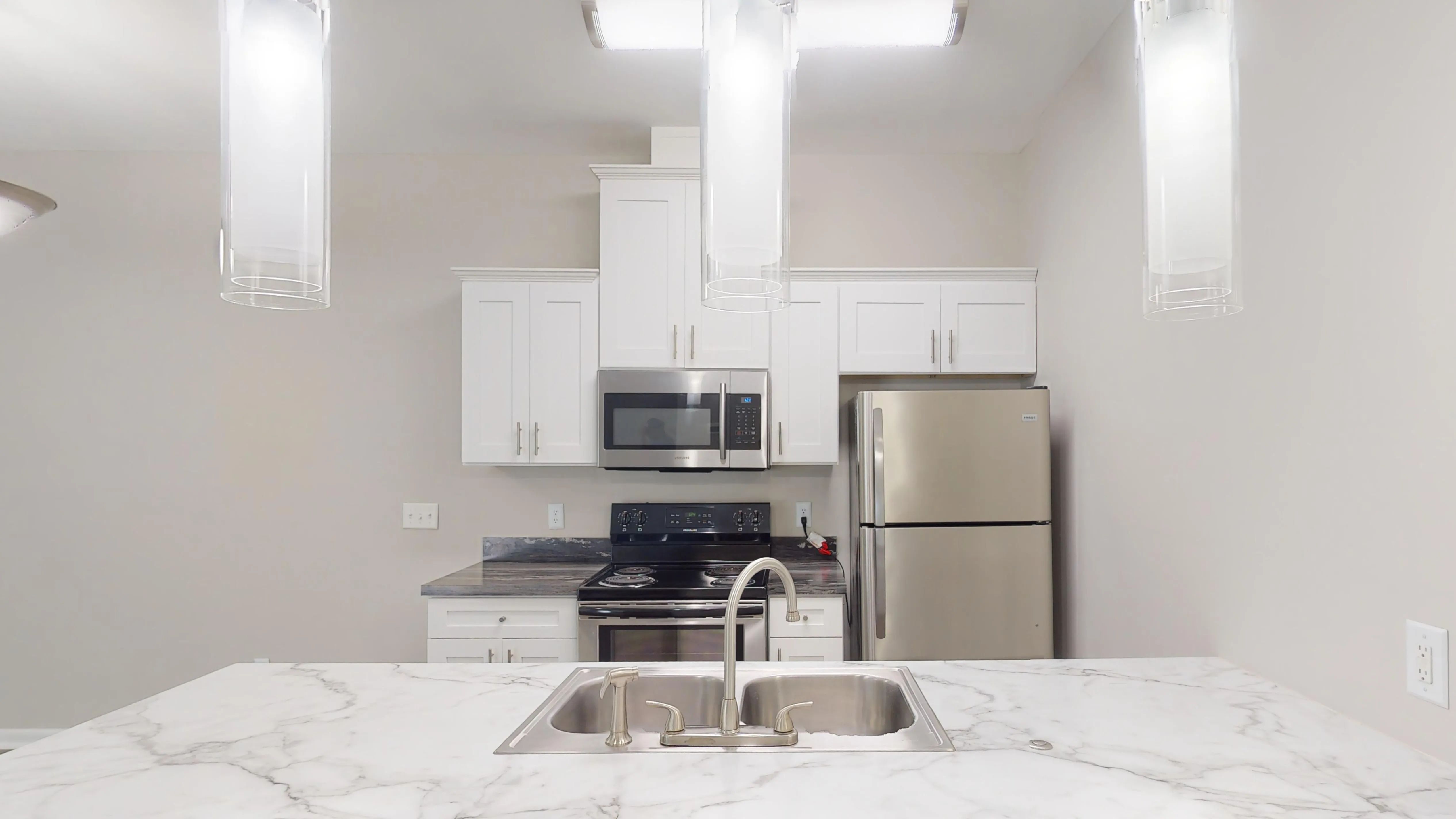 The kitchen in The Rosewood floor plan features stainless steel appliances, bright white cabinetry, marble-inspired countertops, and elegant pendant lighting.