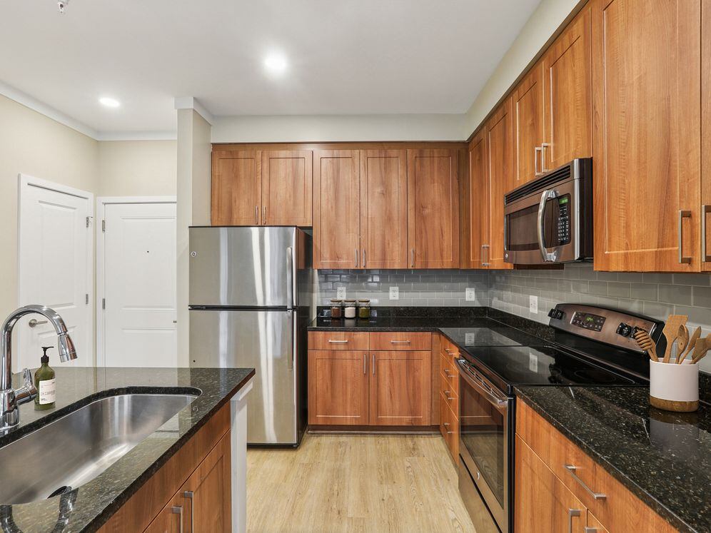 Updated Finishes kitchen with stainless steel appliances, grey tile backsplash, granite countertops, and new hard surface flooring and lighting
