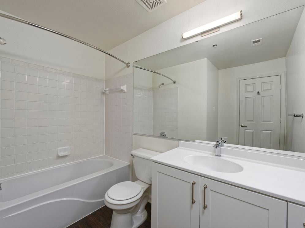 Renovated Package II bath with white cultured marble countertops, white cabinetry, and hard surface flooring