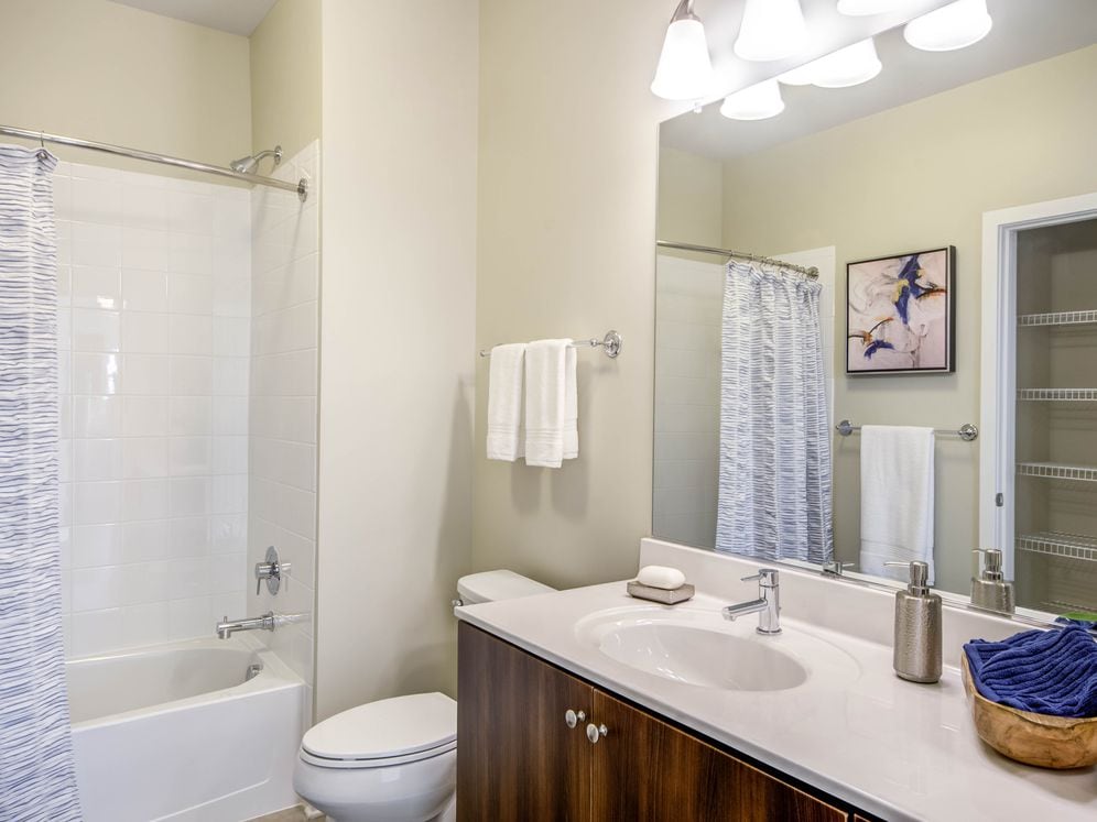 Bathroom with cherry cabinetry, white countertop, linen closet and shower and bath with white tile backsplash