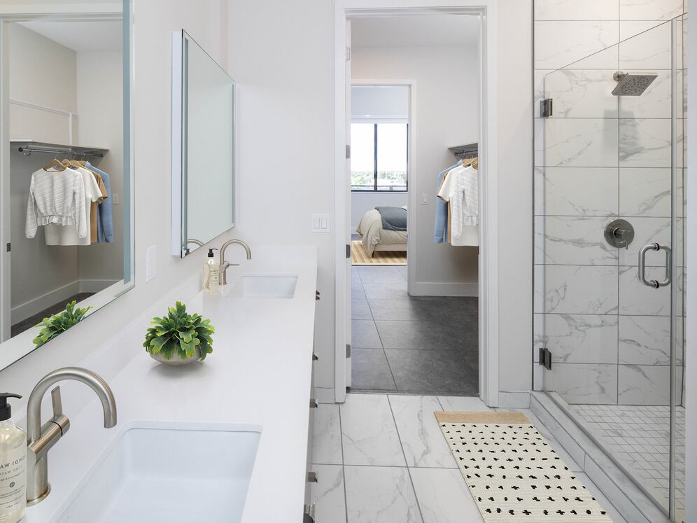 Signature Collection bathroom with grey cabinetry, white quartz countertop, lighted vanity mirrors, porcelain shower surround, and porcelain tile flooring