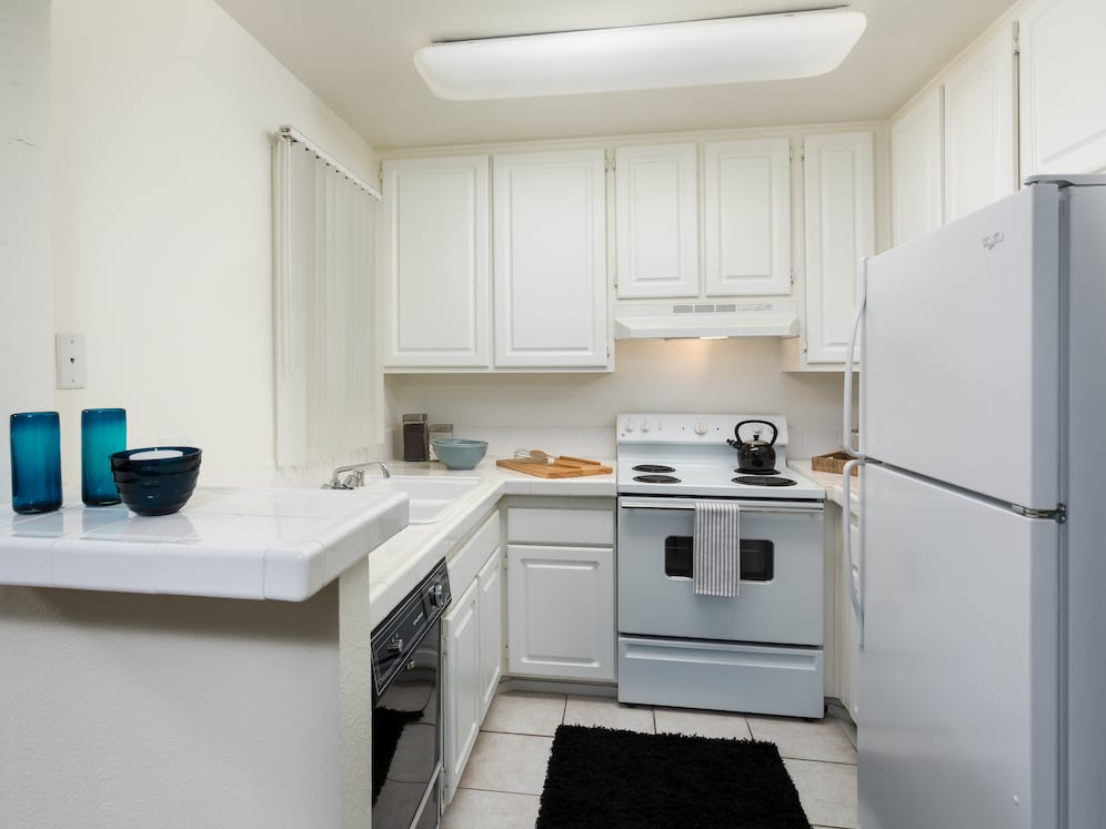 Classic kitchen with white tile countertops, white cabinetry, white appliances, and tile flooring