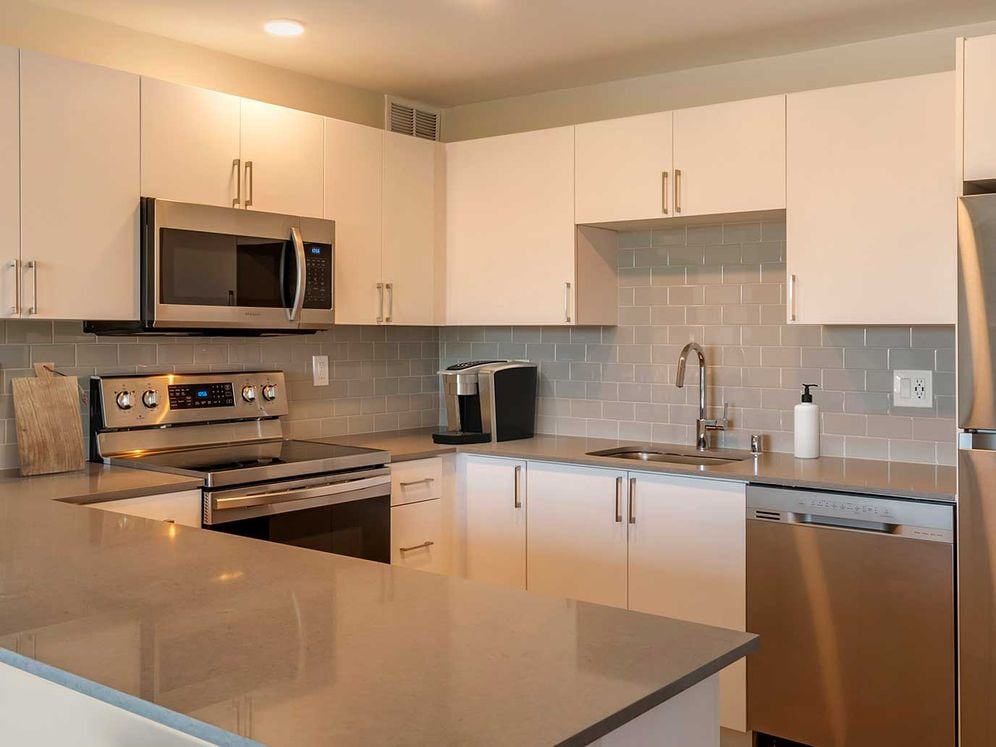 Limited availability: newly renovated Finish Package II apartment homes featuring kitchens with grey quartz countertops, white cabinetry, stainless steel appliances, grey tile backsplash, and hard surface flooring