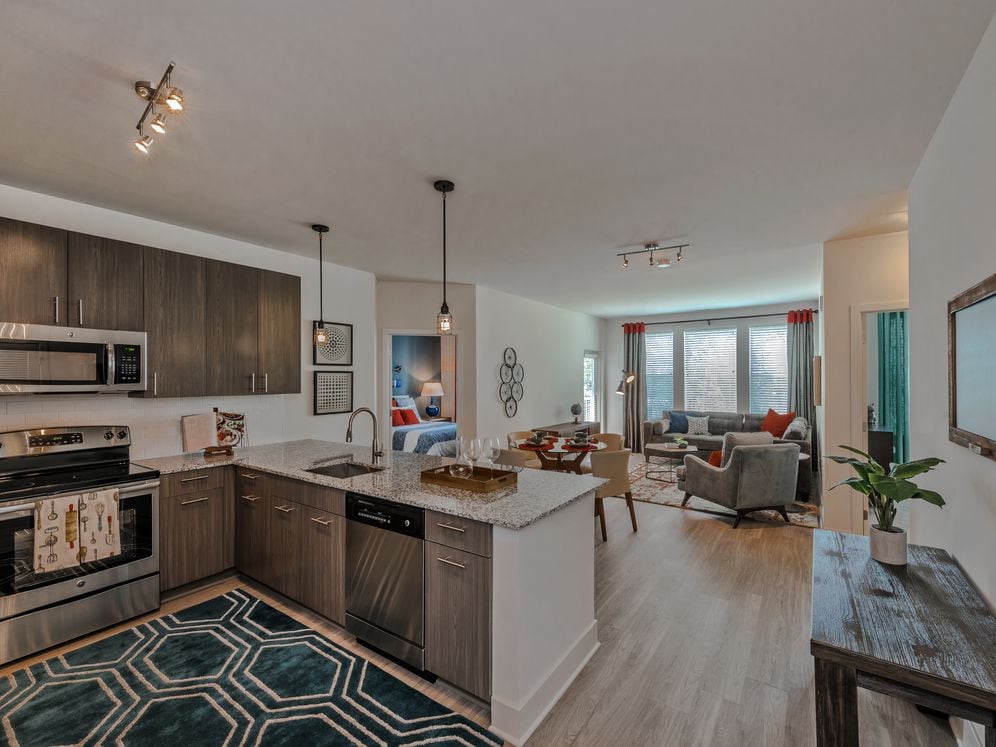 Open concept kitchen with brown cabinetry, granite countertops, stainless steel appliances, tile backsplash and hard surface flooring