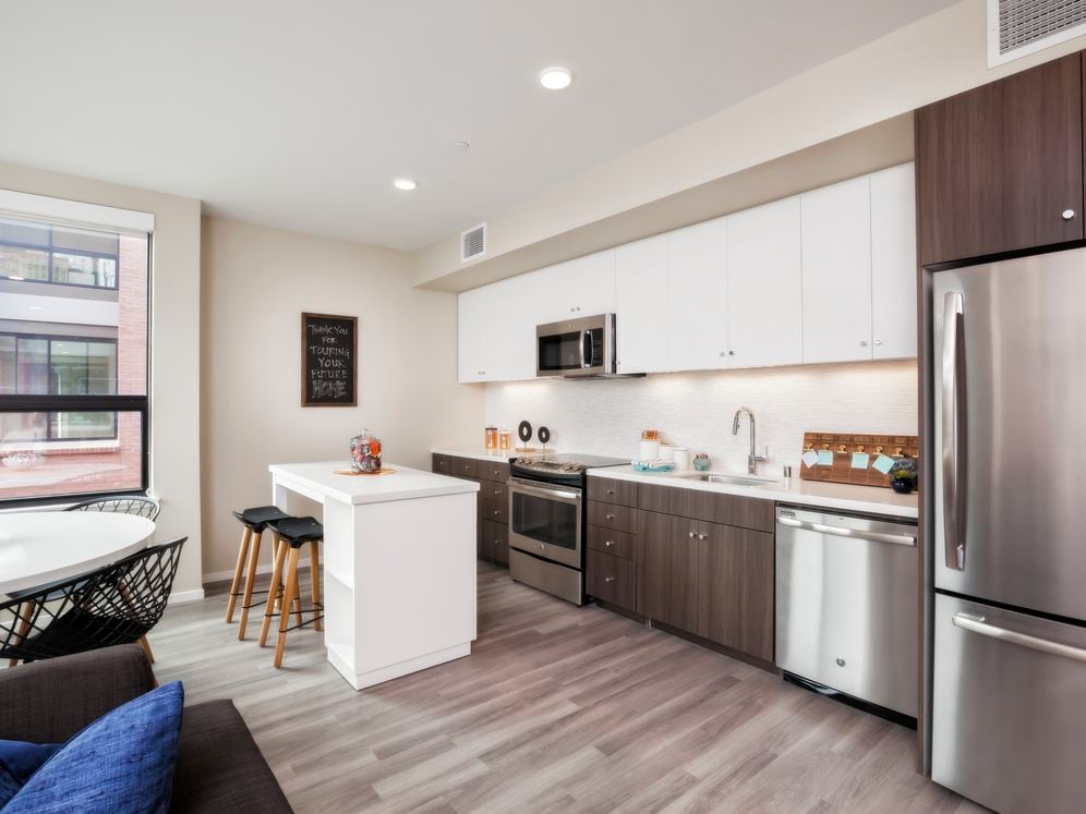 Open concept kitchen with stainless steel appliances, white and brown cabinetry, quartz stone countertop, ceramic tile backsplash, island table and hard surface flooring