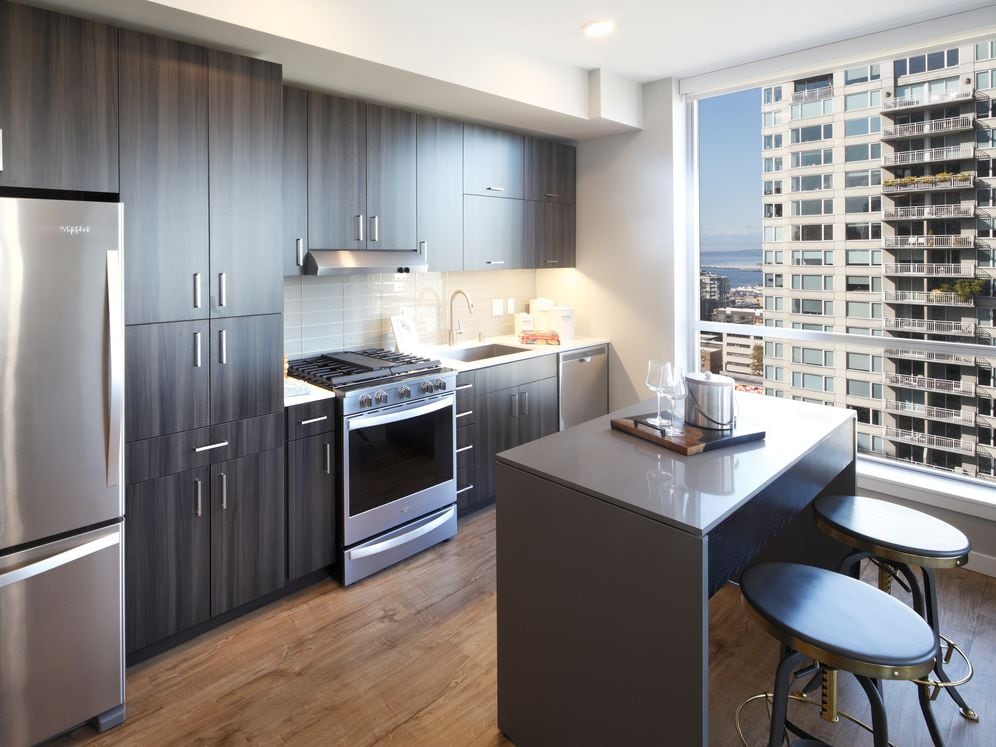 Scheme II kitchen with dark cabinetry and undercabinet lighting, white quartz countertops, glass tile backsplash, stainless steel appliances, and hard surface flooring.