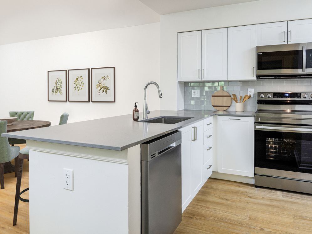 Renovated Package III kitchen with stainless steel appliances, grey quartz countertops (select homes), white cabinetry, light grey tile backsplash, and hard surface flooring