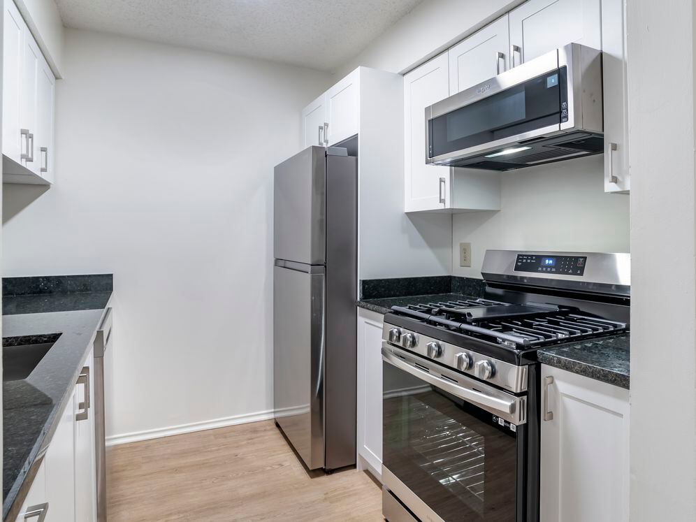 Renovated Package II kitchen with stainless steel appliances, granite countertops, white cabinetry, and hard surface flooring