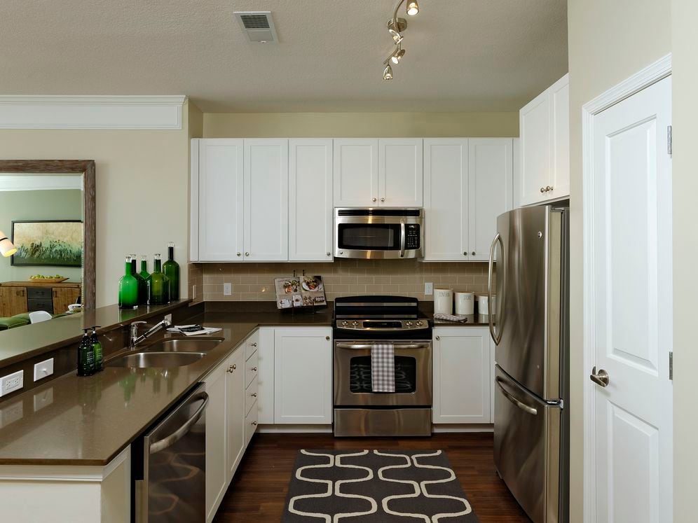 Kitchen with quartz stone countertop, white cabinetry, tile backsplash, stainless steel appliances and hard surface flooring