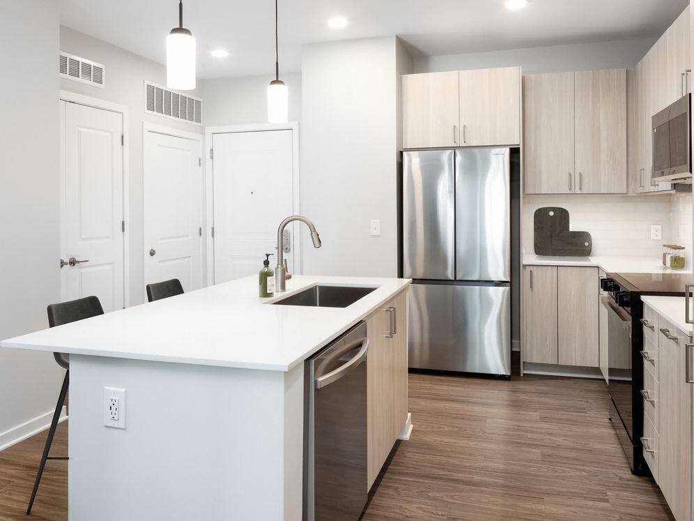 Design Collection II kitchen with stainless steel appliances, cream quartz countertops, oak cabinetry, and hard surface flooring