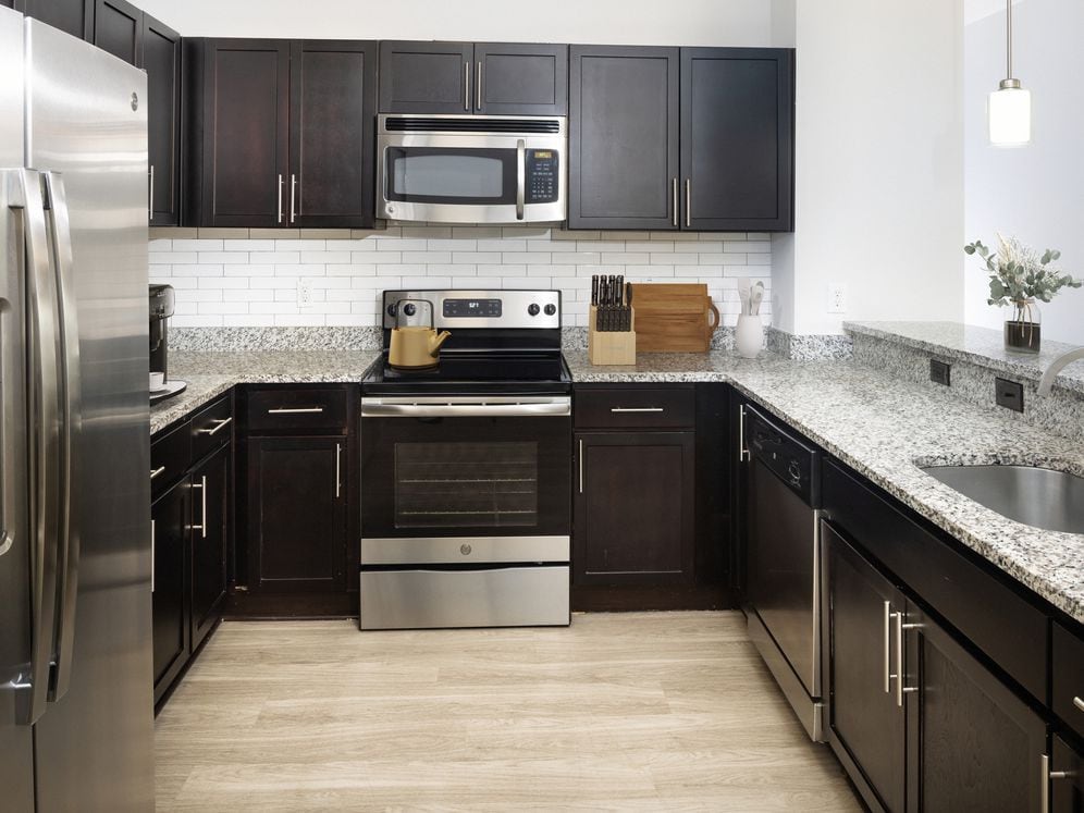 Renovated Package II Kitchen with dark cabinetry, speckled granite countertops, white tile backsplash, stainless steel appliances, pendant lighting, and hard surface flooring