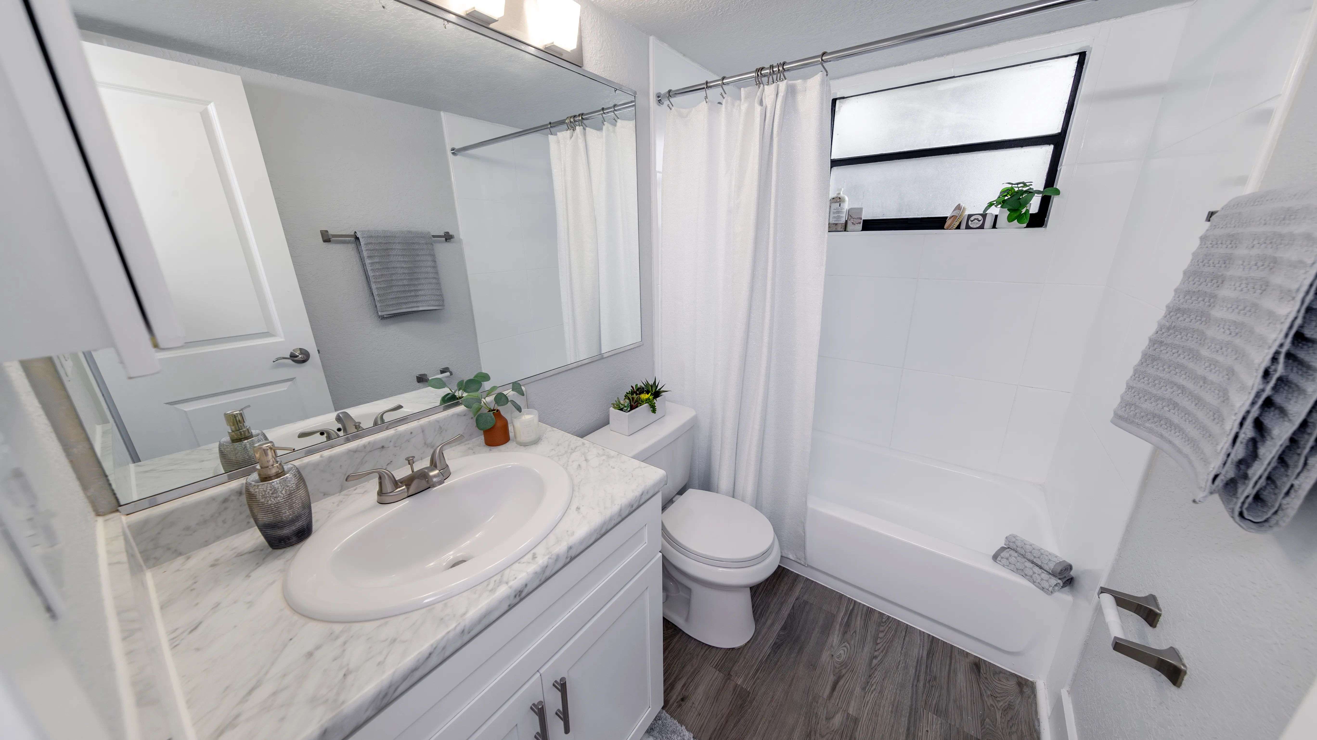 Bright and inviting bathroom featuring sleek white cabinetry, a marble vanity, and wood-style flooring.