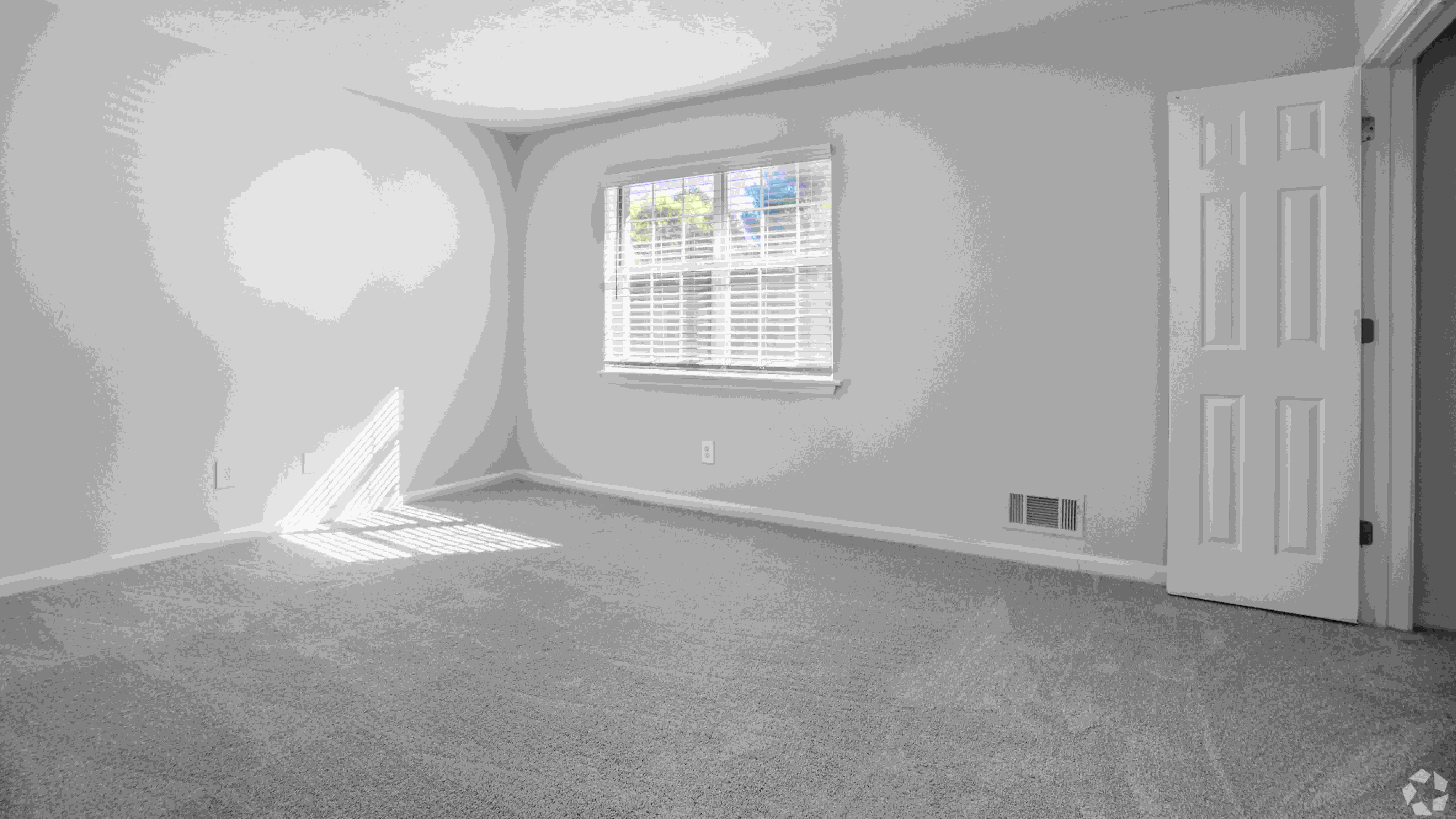 This bedroom in The Roswell floor plan features plush carpeting, a spacious closet, and a large window allowing natural light to shine through.