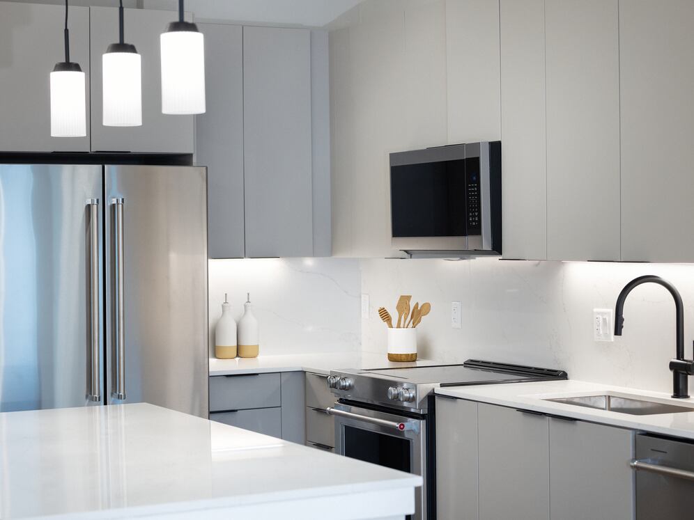 Signature Collection kitchen with stainless steel appliances, light grey cabinetry, marbled quartz countertops and backsplash, under-cabinet lighting, and pendant lighting