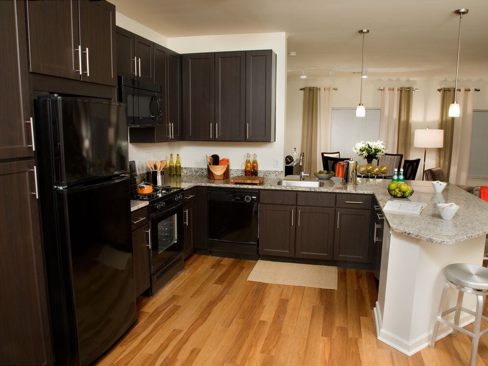 Classic Package kitchen with espresso cabinetry, beige speckled granite countertops, white tile backsplash, black appliances, and hard surface flooring