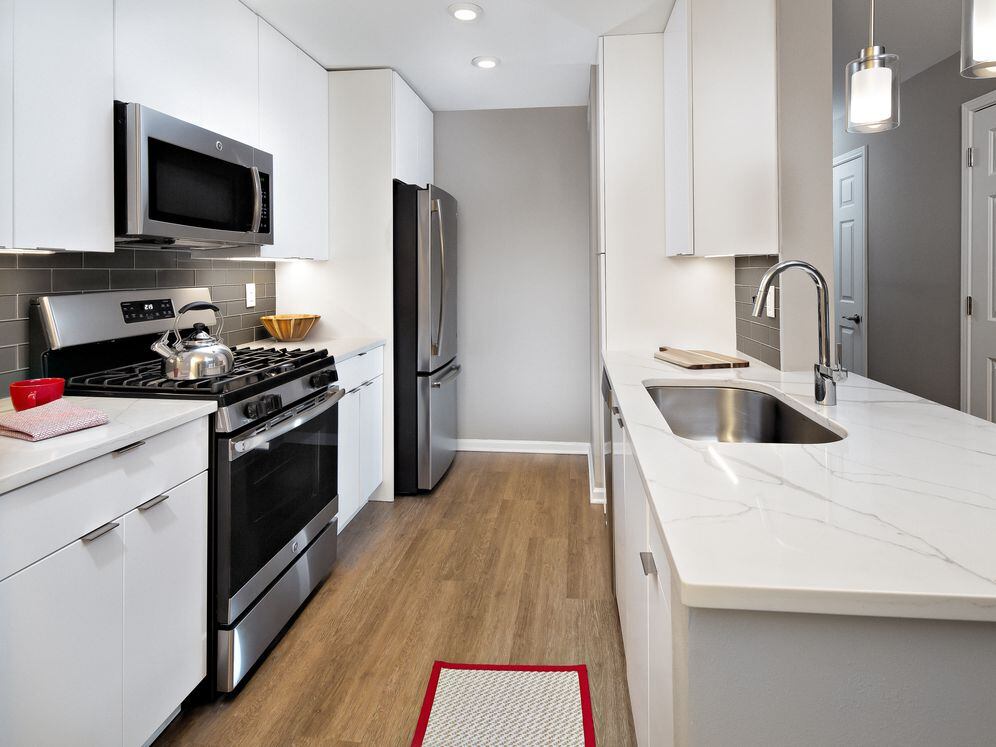 Premier Scheme kitchen with flat white cabinetry, white marbled quartz countertops, grey subway tile backsplash, stainless steel appliances, and hard surface flooring