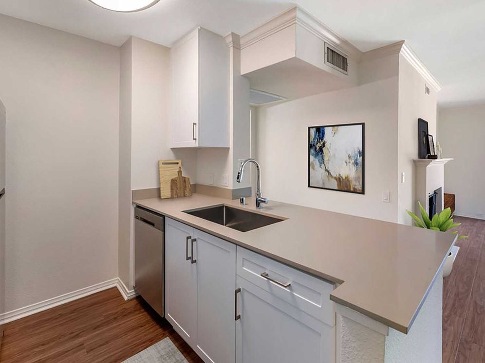 Renovated Package I kitchen with stainless steel appliances, beige quartz countertops, new white cabinetry, and hard surface flooring