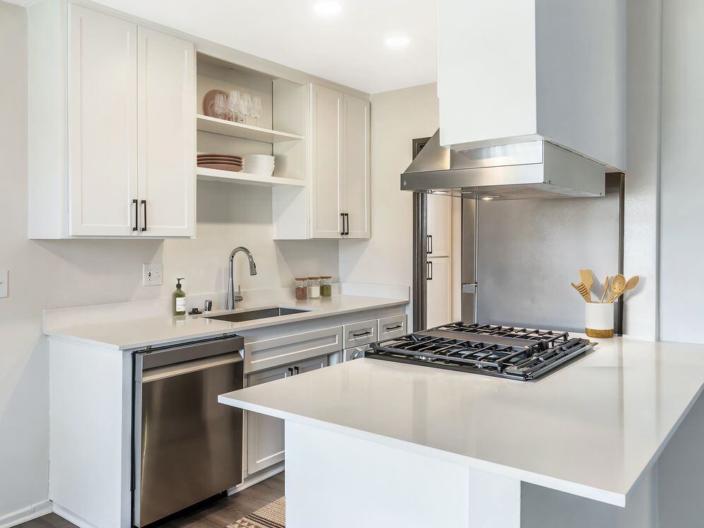 Renovated Package I kitchen with stainless steel appliances, white quartz countertops, white cabinetry, and hard surface flooring (select homes)