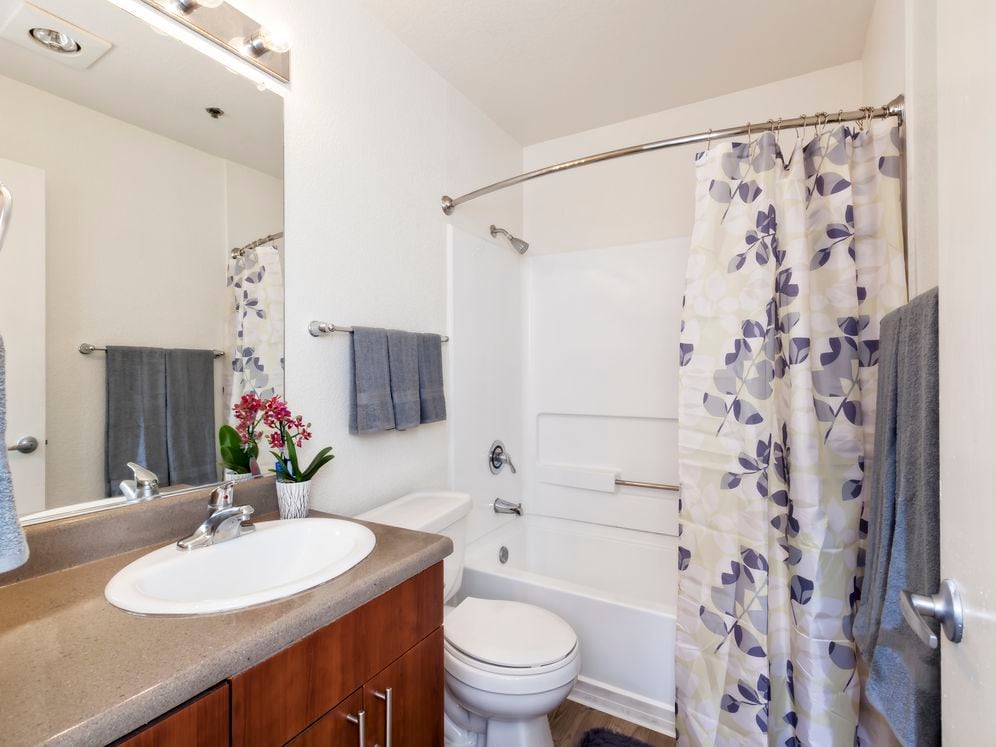 Bathroom with cherry cabinetry, light grey countertop, shower and bath with white tile backsplash