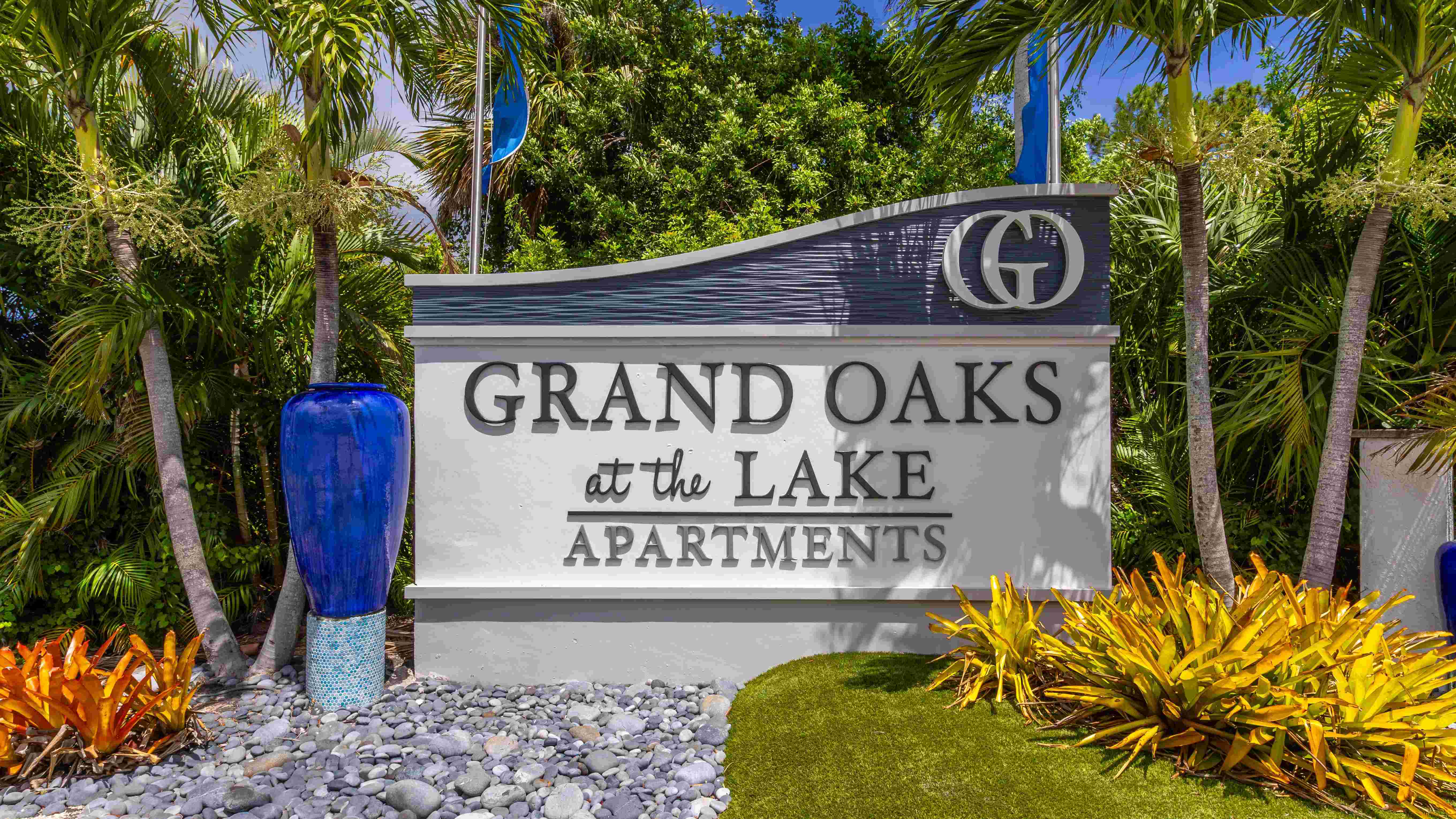Experience the charm of Grand Oaks at the Lake Apartments, where a beautiful entrance framed by tropical landscaping sets the stage for resort-style living.