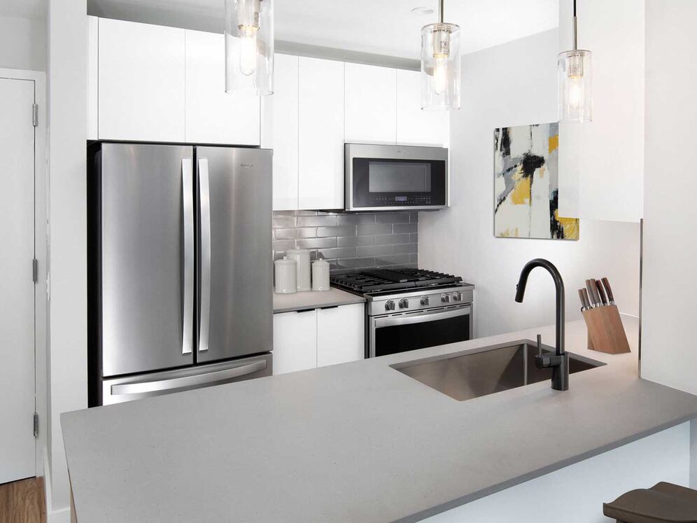 Renovated Package I kitchen with stainless steel appliances, white cabinetry, grey tile backsplash, grey quartz countertops, and hard-surface flooring (Representative Imagery)