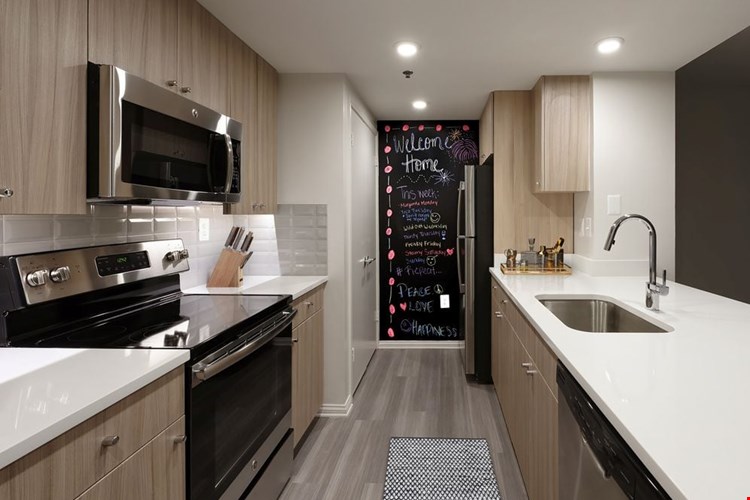 Renovated Package II kitchen with white quartz countertops, white tile backsplash, driftwood cabinetry, stainless steel appliances, and hard surface plank flooring