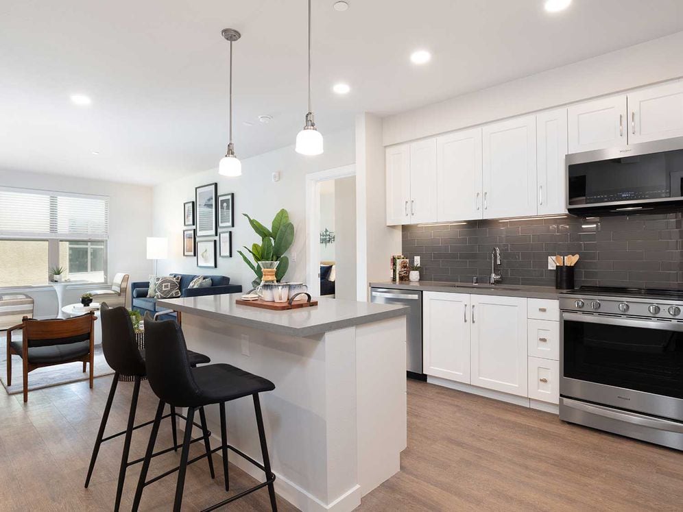 Upgrade Collection kitchen and dining area with stainless steel appliances, white cabinetry, grey quartz countertop, grey tile backsplash, and hard surface flooring