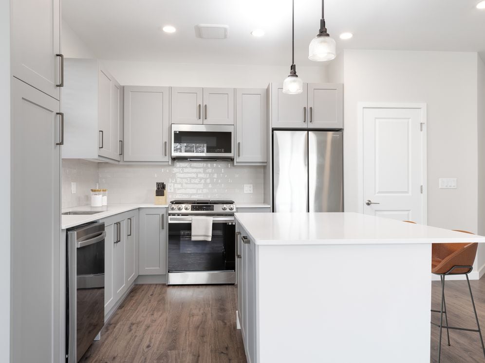 Modern kitchen with stainless steel appliances, white quartz countertop, light grey cabinetry, white tile backsplash, and hard surface flooring