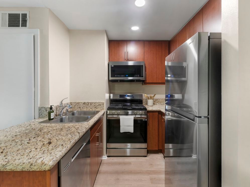 Classic Package II kitchen with stainless steel appliances, beige speckled granite countertops, chestnut cabinetry, and hard surface flooring