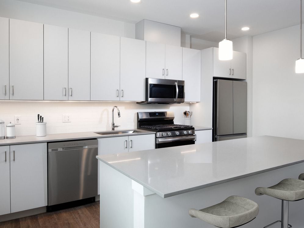 Design Collection I (North Building) Kitchen with light grey cabinetry, white tile backsplash, grey quartz countertops, stainless steel appliances, and hard surface flooring
