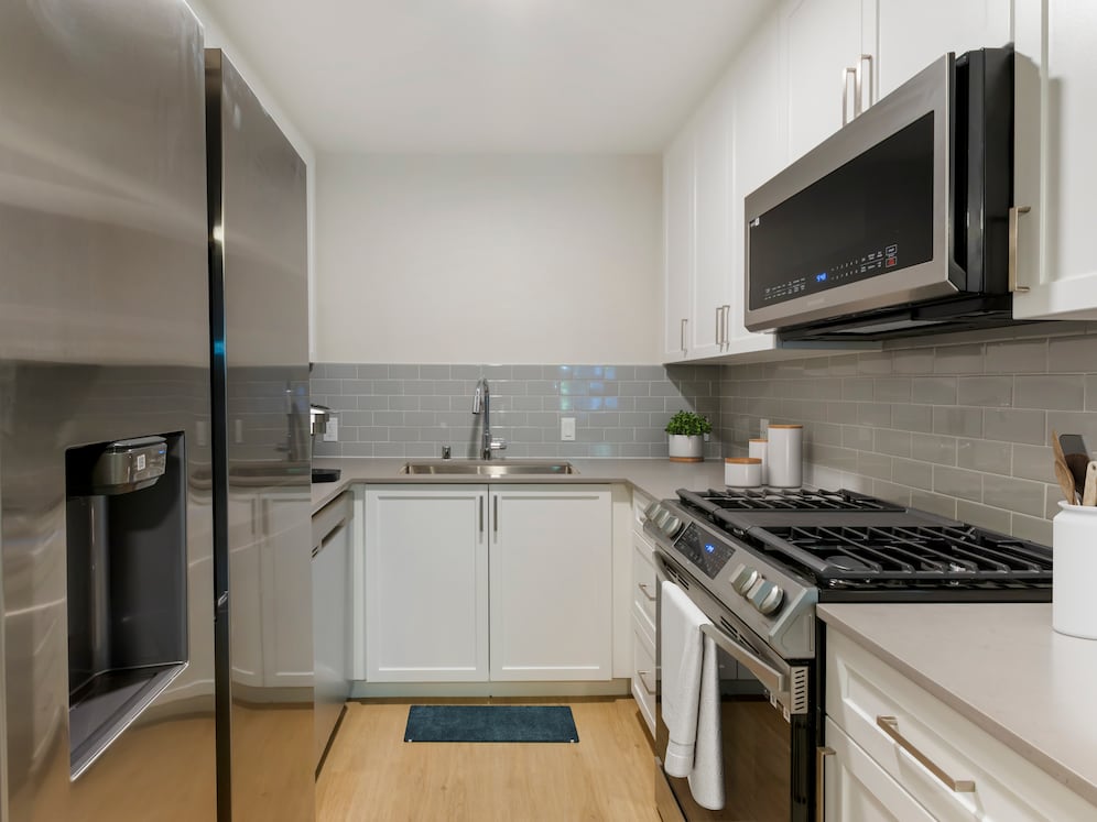 Kitchen with white cabinetry, grey quartz countertops, stainless steel appliances, grey tile backsplash, and hard surface flooring (Select Home)