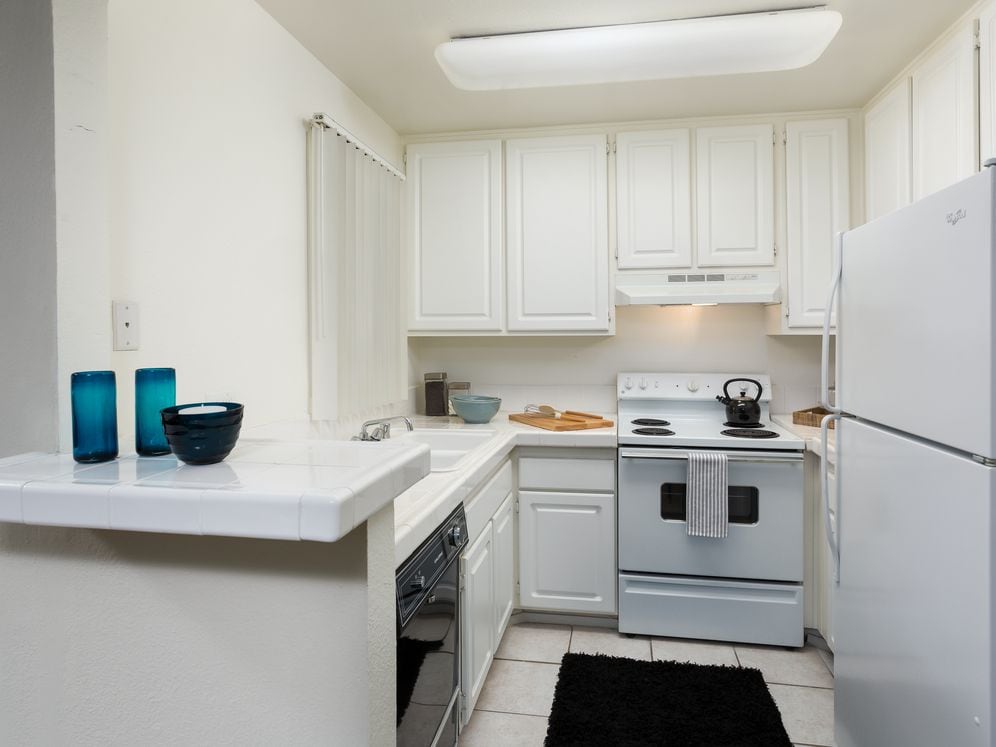 Classic kitchen with white tile countertops, white cabinetry, white appliances, and tile flooring