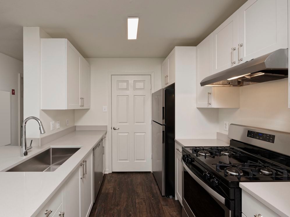 Renovated Package II kitchen with light grey quartz countertops, white cabinetry, stainless steel appliances, and hard surface flooring
