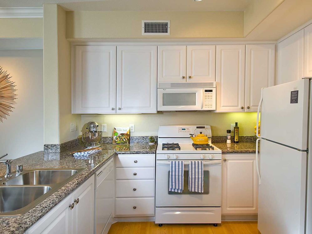 Classic Package I kitchen with white appliances, beige speckled granite countertop, white cabinetry, and hard surface flooring