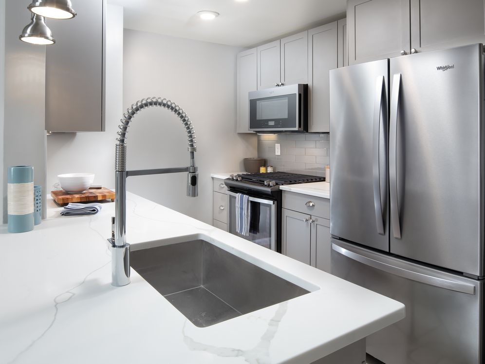 Premier Finish kitchen with grey cabinetry, white quartz countertops, tile backsplash, and stainless steel appliances
