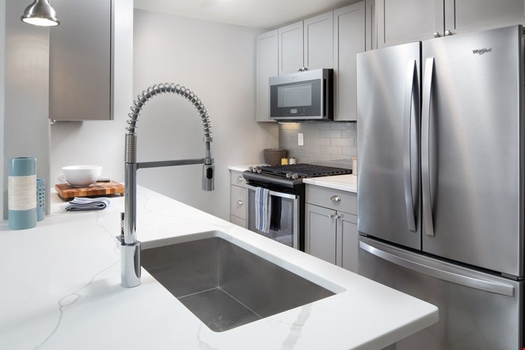Premier Finish kitchen with grey cabinetry, white quartz countertops, tile backsplash, and stainless steel appliances