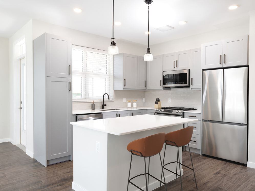 Modern kitchen with stainless steel appliances, white quartz countertop, light grey cabinetry, white tile backsplash, and hard surface flooring