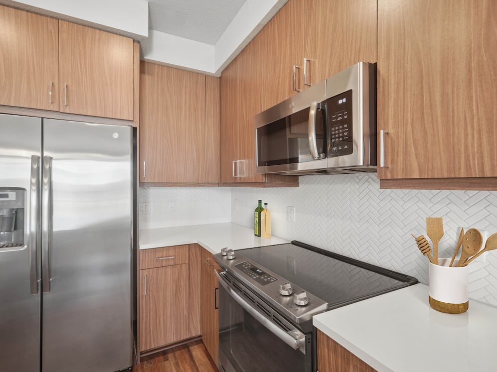 Finish Package I kitchen with stainless steel appliances, dark cabinetry, white tile backsplash, and white quartz countertops