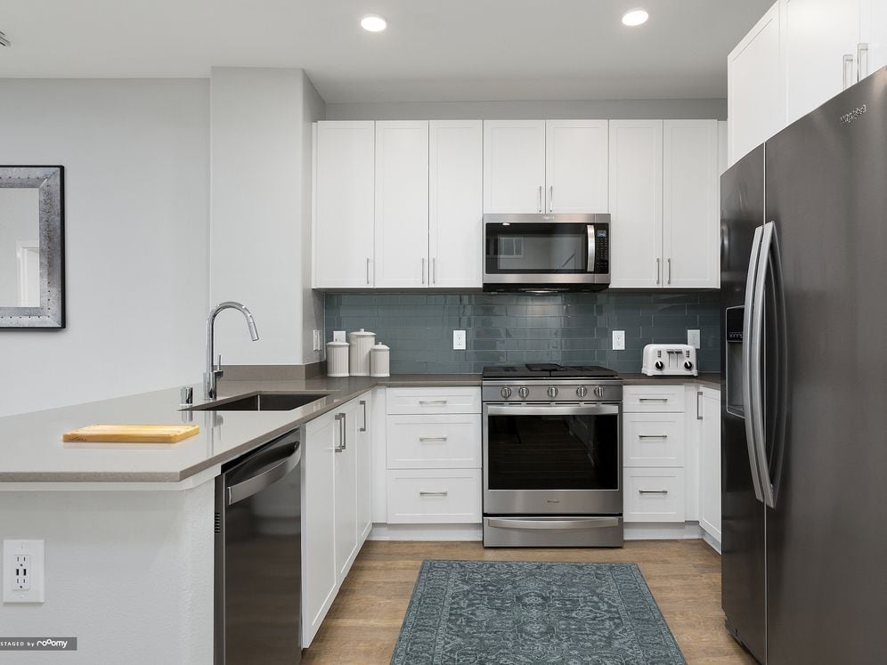Renovated Package I kitchen with white cabinetry, grey quartz countertops, blue/grey tile backsplash, stainless steel appliances, and hard surface flooring