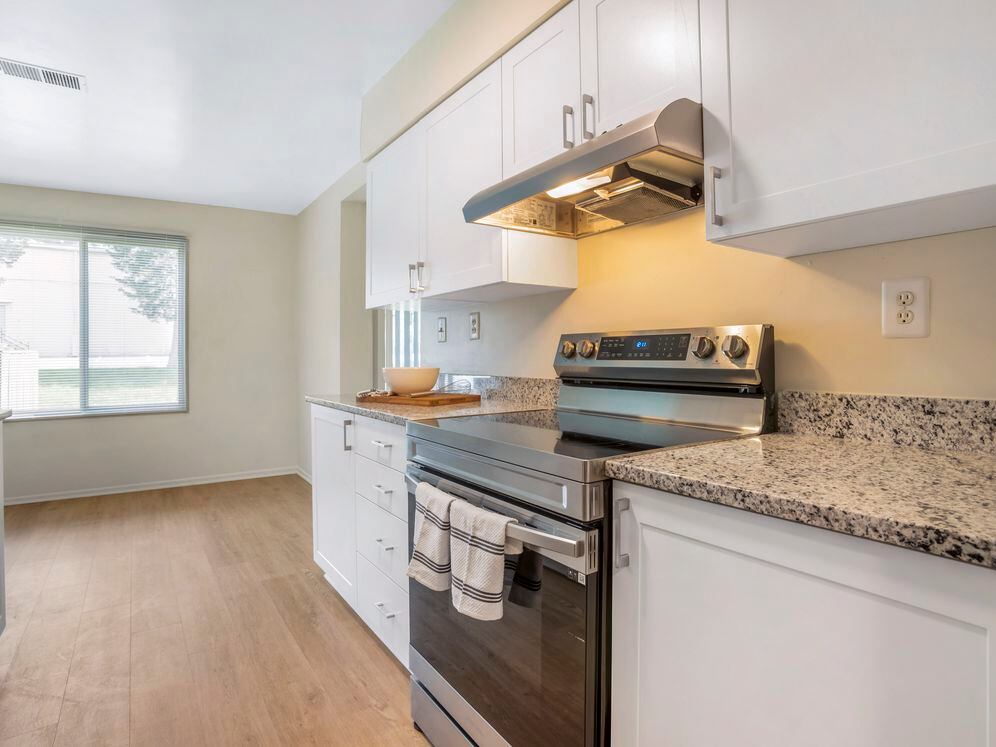 Renovated Package II kitchen featuring stainless steel appliances, white cabinetry, white speckled granite countertops, and hard surface flooring