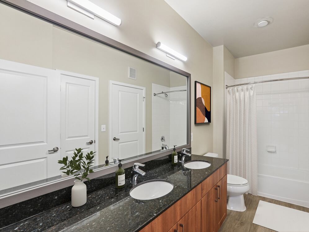Renovated Package I bath with black granite countertop, oak cabinetry, new framed bathroom mirror, and hard surface flooring