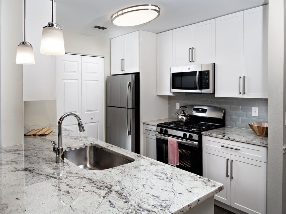 Upgrade Scheme I kitchen with white shaker cabinetry, beige speckled granite countertops, light beige tile backsplash, stainless steel appliances, and hard surface flooring