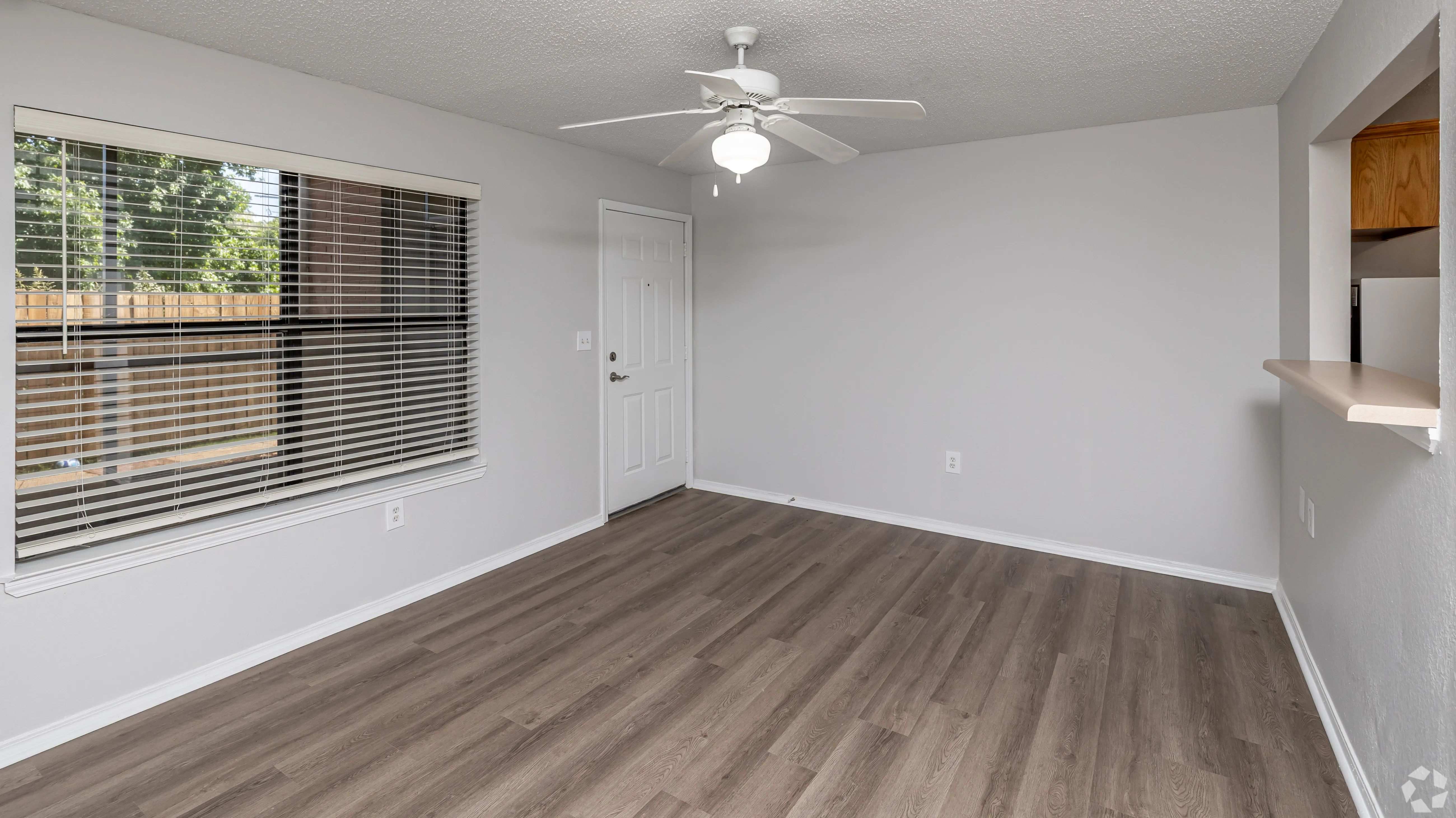 Enjoy a spacious living area featuring wood-style flooring, large windows for natural light, and a ceiling fan to keep things cool.