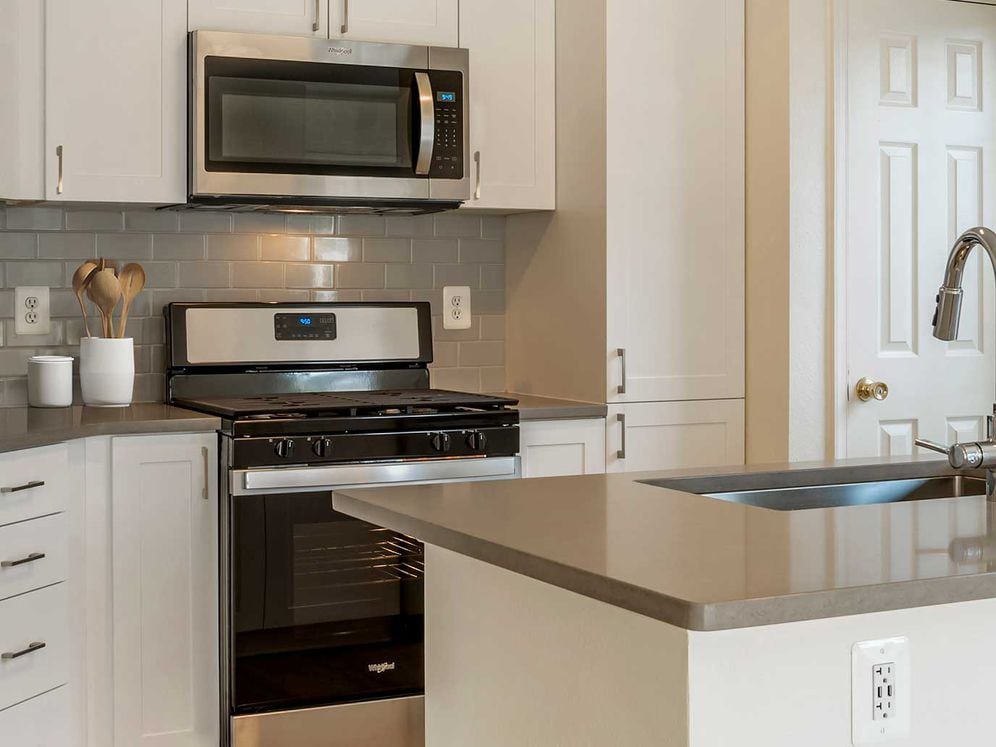 Renovated Package IV kitchens with white cabinetry, grey quartz countertops, stainless steel appliances, grey tile backsplash, and hard surface plank flooring