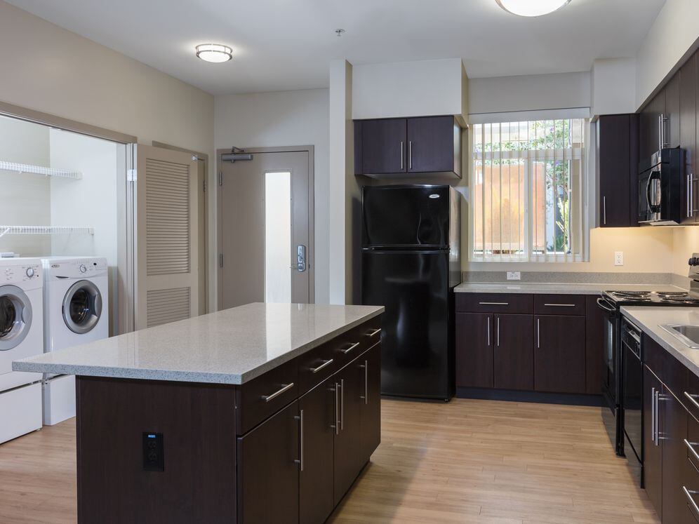 Kitchen with black appliances, grey speckled granite countertops, espresso cabinetry, and hard surface flooring